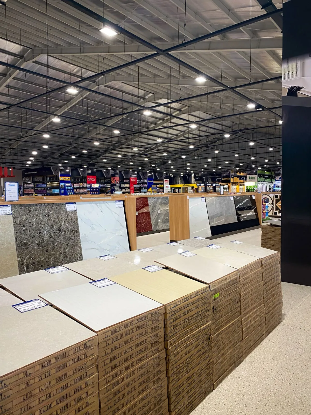 Salão de uma loja de materiais de construção com mostruários de porcelanato e pilhas de caixas de piso